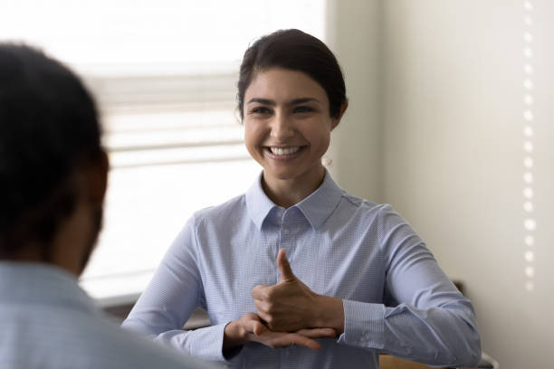 Smiling young Indian woman who is deaf using sign language, communicating with friend or doctor physician, happy attractive female having fun and enjoying pleasant conversation, hard of hearing
